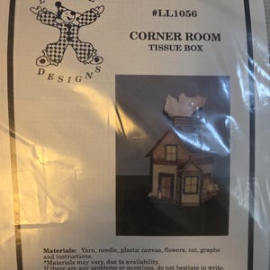 May include: A craft kit for a Corner Room Tissue Box, featuring a small house design. The packaging includes the text "LuvLee Designs" and "#LL1056". The kit includes yarn, needle, plastic canvas, flowers, cat, graphs, and instructions.