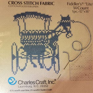 May include: Cross stitch fabric with a blue carriage design. The fabric is cotton, polyester, and linen blend. The package includes a 12" x 18" piece of 14-count Fiddler's "Lite" fabric. The text "Charles Craft, Inc." is visible.