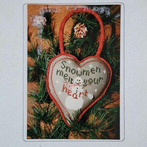 May include: Cross stitch pattern for a heart-shaped ornament with a snowman and the text "Snowmen melt your heart". The pattern is from Hillside Samplings.