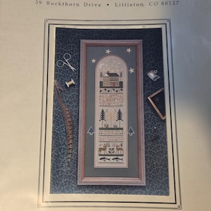 May include: A cross-stitch sampler kit titled "North Country Sampler" by The Drawn Thread. The design features a house, trees, deer, fish, and an alphabet. The kit includes the address 39 Buckthorn Drive, Littleton, CO 80127.