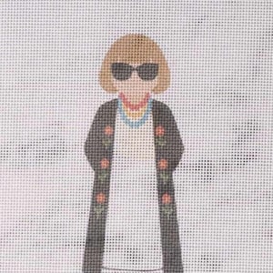 May include: Needlepoint canvas featuring a stylized figure with sunglasses, a bob haircut, and a black coat adorned with floral accents. The figure wears a colorful necklace and a white dress. The background is a white grid.
