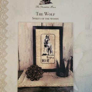 May include: A cross-stitch pattern featuring a wolf with the text "Lupus Wolf" in a black frame. The pattern is titled "The Wolf - Spirits of the Woods" and is by The Primitive Hare.