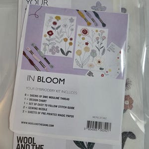 May include: An embroidery kit by Wool and the Gang titled In Bloom. The packaging includes 6 skeins of DMC Mouliné thread, a design chart, a stitch guide, 2 sewing needles, and 2 sheets of pre-printed magic paper with floral designs.