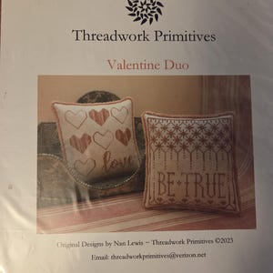 May include: A package featuring two cross-stitch pillow designs. One pillow has hearts and the word "love", the other says "BE TRUE". The package is labeled "Valentine Duo" by Threadwork Primitives.