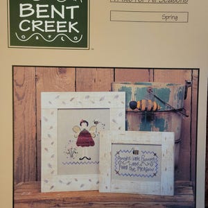 May include: Cross stitch pattern for a spring-themed pixie with the text "Awake little flowers and Paint the Meadow". The pattern is from Bent Creek and is part of a series called "A Pixie For All Seasons".