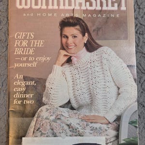 May include: A vintage magazine cover for "The Workbasket" from May 1989. The cover features a woman wearing a white crocheted sweater and floral skirt. Text includes "Gifts for the Bride" and "An elegant, easy dinner for two."