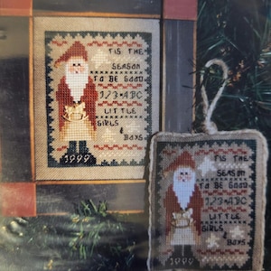 May include: A cross-stitch pattern featuring a Santa Claus holding a gift. The pattern includes the text "Tis the season to be good 123 ABC Little girls & boys".