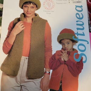 May include: Two knitted vests, one green and one orange, with matching hats. The vests are shown on two people, one adult and one child. The text on the page reads "Berroco Softwear", "Original Designs", "Expanded Size Range", "Exclusive 10 Brochure #197", "Soft and cozy knits for girls of all sizes in Plush, X-pre Paparazzi and", "SKU: 0021990 $ 7.98", "YP 0000", "DP 100".