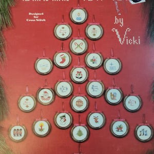 May include: A red Christmas-themed cross-stitch pattern featuring a tree shape made of framed ornaments. Each ornament has a different holiday design, including a snowman, Santa, and a Christmas tree. The text "Christmas Doo-Dads" is at the top.