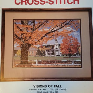 May include: Framed cross-stitch artwork titled "VISIONS OF FALL." The image depicts a fall landscape with a church and trees with orange and yellow leaves. The finished size is 9 3/4" x 13 1/2". The text "HOLBERT CROSS-STITCH" is at the top.