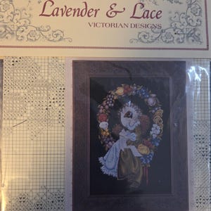 May include: A cross-stitch kit featuring a Victorian design. The kit includes a framed image of a figure surrounded by a floral wreath. The text "Lavender & Lace" and "Victorian Designs" are visible on the packaging.