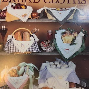 May include: A promotional image for holiday bread cloths. The image features various baskets filled with bread and other items, each lined with decorative cloths. The cloths have embroidered designs, and the image includes text that reads "Holiday Bread Cloths."