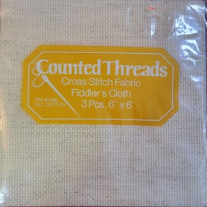 May include: A package of three 6-inch by 6-inch pieces of white cotton Aida cloth for cross stitch, labeled "Counted Threads Cross Stitch Fabric Fiddler's Cloth 3 Pcs. 6" x 6" RN 45156 ALL COTTON".