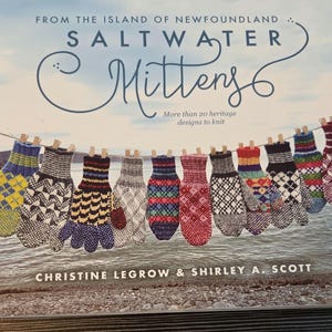 May include: A book titled From the Island of Newfoundland Saltwater Mittens by Christine LeGrow and Shirley A. Scott. The cover features a row of colorful, patterned knit mittens hanging on a clothesline above a rocky shoreline.