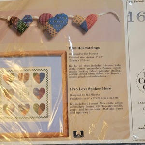 May include: A cross-stitch pattern kit for a heart-shaped design with the text "Love Spoken Here". The kit includes 11-count Aida cloth, cotton embroidery floss, a tapestry needle, a graph, and instructions. The finished size is 9 inches by 9 inches.