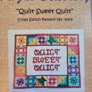 May include: A cross-stitch pattern titled "Quilt Sweet Quilt" by Rogue Stitchery. The design features a central text box with the words "Quilt Sweet Quilt" in red, surrounded by a border of colorful quilt block patterns. The background is a tan fabric.
