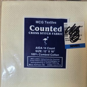 May include: Cream-colored Aida cross stitch fabric, 12" x 18", with a dark blue label. The label reads "MCG Textiles Counted Cross Stitch Fabric" and includes instructions for counted cross stitch and charted alphabet for monogramming.