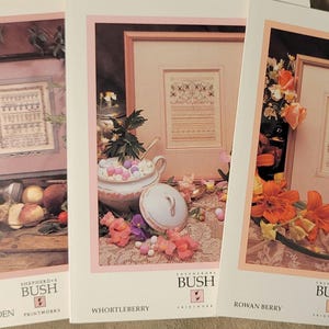 May include: Three cross-stitch patterns featuring floral designs and the text "Shepherd's Bush" with the names of the patterns "The Root Garden", "Whortelberry", and "Rowan Berry".