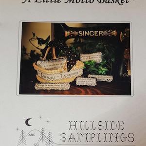 May include: A close-up of a cross-stitch pattern for a small basket with various inspirational mottos, including "Live Well, Laugh Often" and "Practice random acts of kindness". The pattern is displayed on a vintage Singer sewing machine.