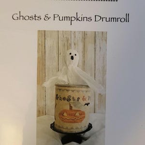 May include: A cross stitch pattern featuring a ghost and a pumpkin on a vintage-style can. The pattern is titled "Ghosts & Pumpkins Drumroll" and is designed by Rebecca Noland.