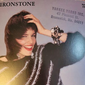 May include: A woman with short dark hair is wearing a black and white striped sweater with a fuzzy texture. She is wearing a silver bracelet with beads and a pair of silver earrings. The image is from a knitting pattern book. The text on the image reads "IRONSTONE", "Style 478", "YANKEE YARNS INC.", "47 Pleasant St.", "Brunswick, Me. 04011".