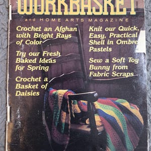 May include: The cover of "The Workbasket" magazine from April 1985. The cover features a wooden chair draped with a colorful crocheted afghan. Text includes "Crochet an Afghan with Bright Rays of Color" and "Knit our Quick, Easy, Practical Shell in Ombre Pastels."