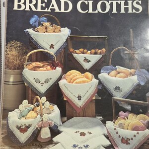 May include: A leaflet titled "Mimi's Country Bread Cloths" featuring various bread cloths in baskets. The cloths are white with embroidered designs of houses, hearts, and animals. Baskets are filled with bread and decorative dolls.