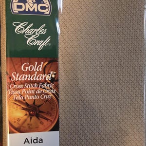 May include: Beige Aida cross stitch fabric, 15 x 18 inches, with a count of 14. The packaging features the "Gold Standard" and "DMC" logos, along with the text "Cross Stitch Fabric".