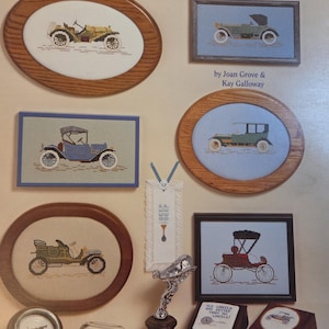 May include: A collection of cross-stitch patterns and decorative items featuring antique cars. The designs include framed pictures, a silver car hood ornament, and small wooden boxes. The text "Antique Cars" is at the top.