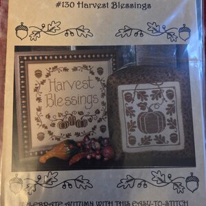 May include: A cross-stitch pattern packet titled "#130 Harvest Blessings" featuring two autumn-themed designs. One design is framed, the other is a pillow. The packet includes the text "Celebrate Autumn with this easy-to-stitch pair of harvest designs!"