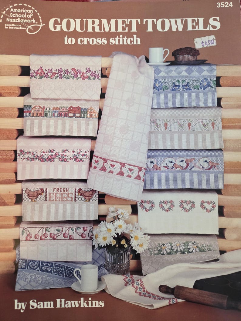 May include: A selection of cross-stitch gourmet towels featuring diverse designs such as flowers, houses, chickens, cherries, and hearts. The towels are arranged on a wooden surface, with the text "GOURMET TOWELS to cross stitch" displayed.