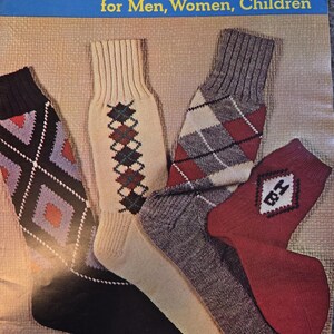 May include: An assortment of hand-knit socks in various colors and patterns, including argyle and diamond designs. The image features socks in black, cream, gray, and red. Text at the top reads "Hand Knit Socks for Men, Women, Children."