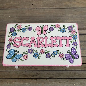 May include: A white wooden step stool with a pink border and a painted design of flowers, butterflies, and the name "SCARLETT".