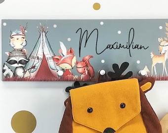 May include: A wooden coat rack with a gray background and a woodland animal theme. The rack features a fox, a deer, a raccoon, and a teepee. The text "Maximilian" is written on the rack. A small, yellow, deer-shaped backpack hangs from the rack. A wooden sign with the text "sweet dreams" hangs below the rack.