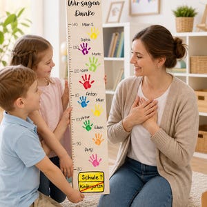 Pode incluir: Um gráfico de crescimento de madeira com impressões de mãos coloridas e nomes, com "Wir sagen Danke" no topo. Crianças e um adulto estão reunidos em torno do gráfico. O gráfico mede em centímetros.