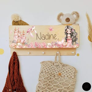 Peut inclure: Un porte-manteau en bois avec une plaque de nom personnalisée représentant une sirène, une tortue de mer et un château. La plaque de nom indique "Nadine".