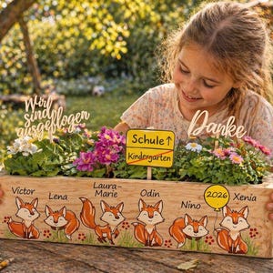 Pode incluir: Uma floreira de madeira com um desenho de raposa pintada, cheia de flores coloridas. A caixa tem nomes e o texto "Schule ↑ Kindergarten" e "Danke". Uma menina segura a floreira.
