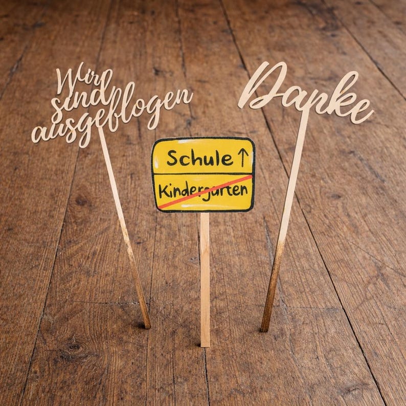 May include: Wooden signs with the phrases "Wir sind ausgeflogen" and "Danke" in cursive script. A yellow sign with "Schule" and "Kindergarten" crossed out is also present. The signs are on wooden sticks, set against a wooden background.