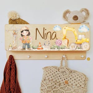 Peut inclure: Panneau mural en bois sur le thème de la construction, avec une fille en gilet de chantier, une grue et une excavatrice jaune. Comprend le nom "Nina" et des chevilles pour accrocher des objets.