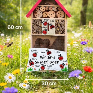 May include: A wooden insect hotel, 60 cm tall and 30 cm wide, with a red roof and a sign that says "Kindergarten". The hotel is filled with various natural materials and has a sign with names and ladybug illustrations. The text "Wir sind ausgeflogen" is also visible.
