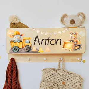 Peut inclure: Porte-manteau mural en bois avec le nom "Anton" et des illustrations sur le thème de la construction. Comprend un rhinocéros dans un camion, un ours sur un bulldozer et des guirlandes décoratives.