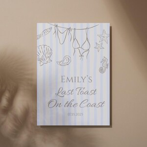 Puede incluir: Un letrero rectangular con un fondo a rayas azules y blancas. El letrero presenta dibujos lineales de conchas marinas, un bikini y estrellas de mar. El texto "EMILY'S Last Toast On the Coast" se muestra en una elegante escritura, con la fecha 07.15.2025 debajo.