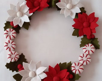 May include: A Christmas wreath made of felt with red and white poinsettia flowers, green holly leaves, and red and white candy canes.