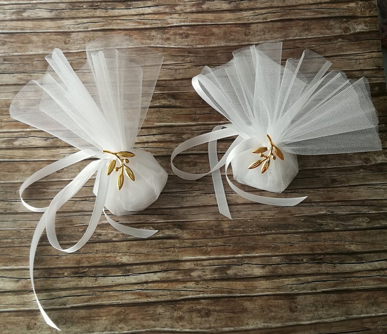 May include: Two white tulle favor bags with gold olive branch accents tied with white satin ribbon.