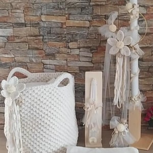May include: A white crocheted basket with a white flower and tassel, a white towel, and a white candle with a white flower and tassel decoration.
