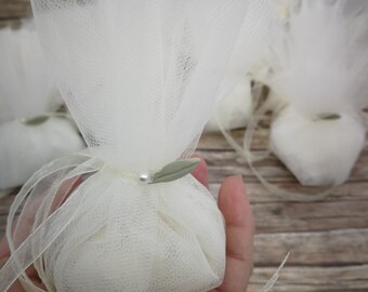 Puede incluir: Bolsas de regalo de tul blanco con una pequeña hoja verde y un acento de perla. Las bolsas están atadas con una cinta de satén blanco.