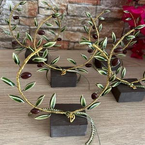 May include: Four small olive branch sculptures with green leaves and brown olives, each on a black square base. The branches are made of wire and have a gold finish.