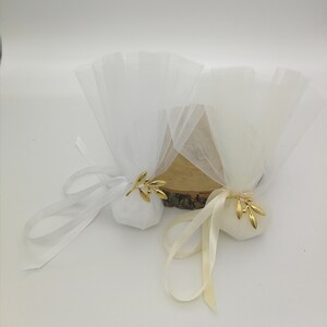 May include: Two white tulle favor bags with gold olive branch accents. The bags are tied with white and cream satin ribbon.