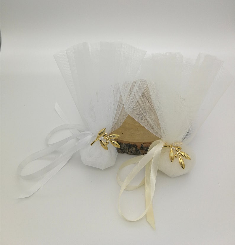 May include: Two white tulle favor bags with gold olive branch accents. The bags are tied with white and cream satin ribbon.