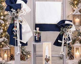 May include: A set of baptismal candles and a white cloth with navy blue trim, decorated with nutcracker ornaments, pinecones, and gold star accents. The items feature thick white rope detailing and are arranged with a small glass bottle.